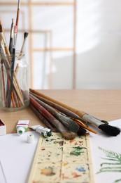 Photo of Different brushes, colorful paints, palette and drawing on table in studio. Artist's workplace
