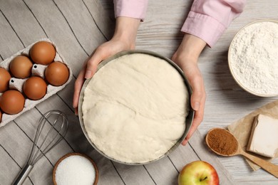 Photo of Woman holding bowl with fresh yeast dough and ingredients for cake on wooden table, closeup