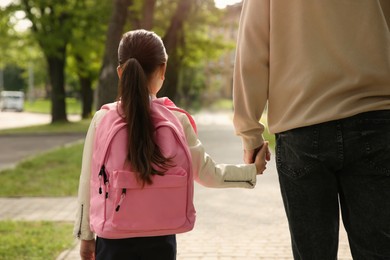 Photo of Father taking his little daughter to school through park, back view