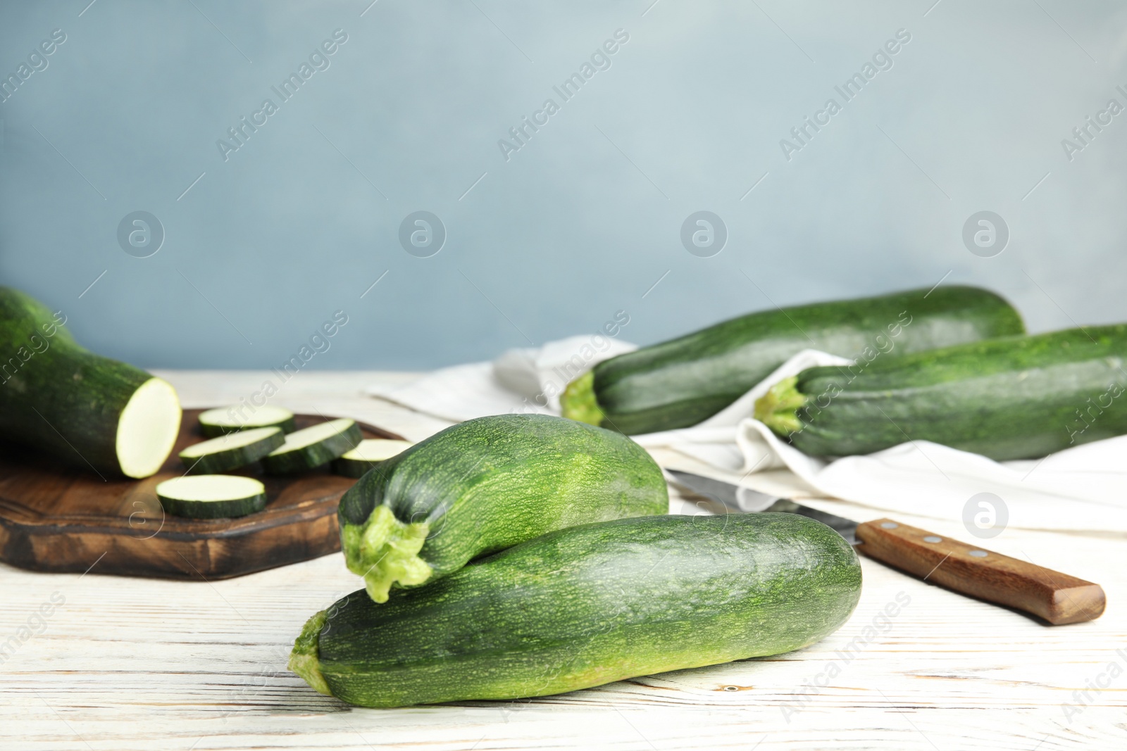 Photo of Fresh ripe green zucchinis on white wooden table against blue background, space for text