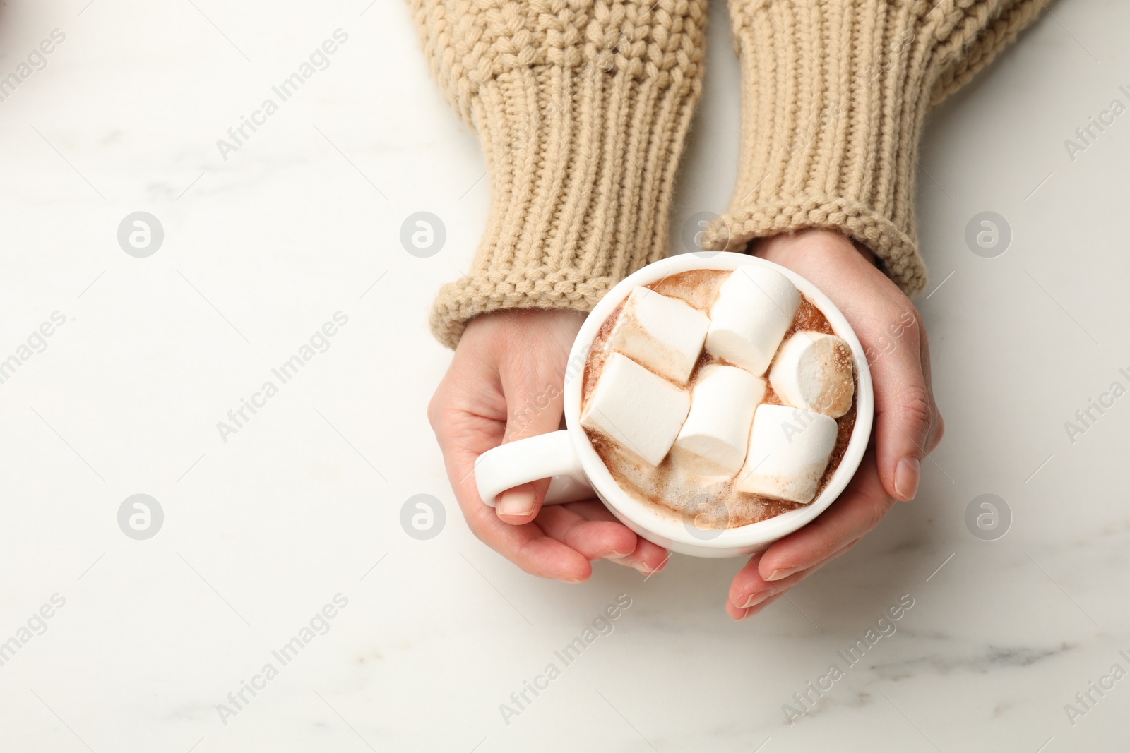 Photo of Woman with cup of tasty hot chocolate and marshmallows at white marble table, top view. Space for text