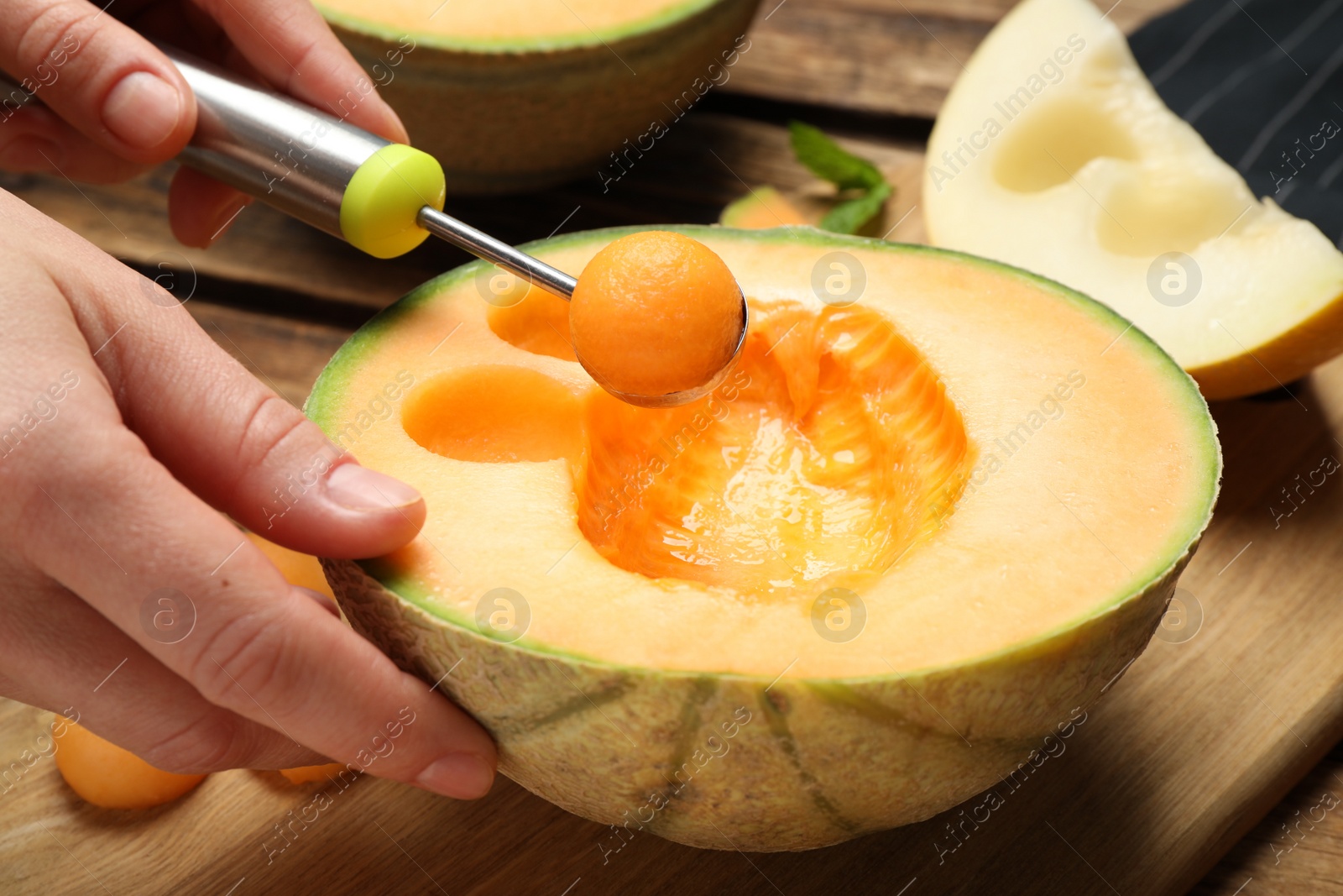 Photo of Woman making melon balls at wooden table, closeup