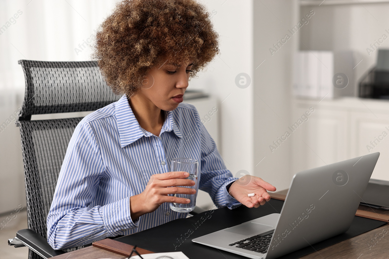 Photo of Woman with pill and glass of water suffering from headache at workplace in office