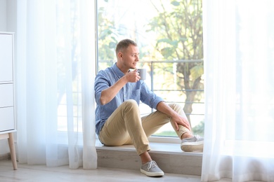 Young man having rest near window with open curtains at home