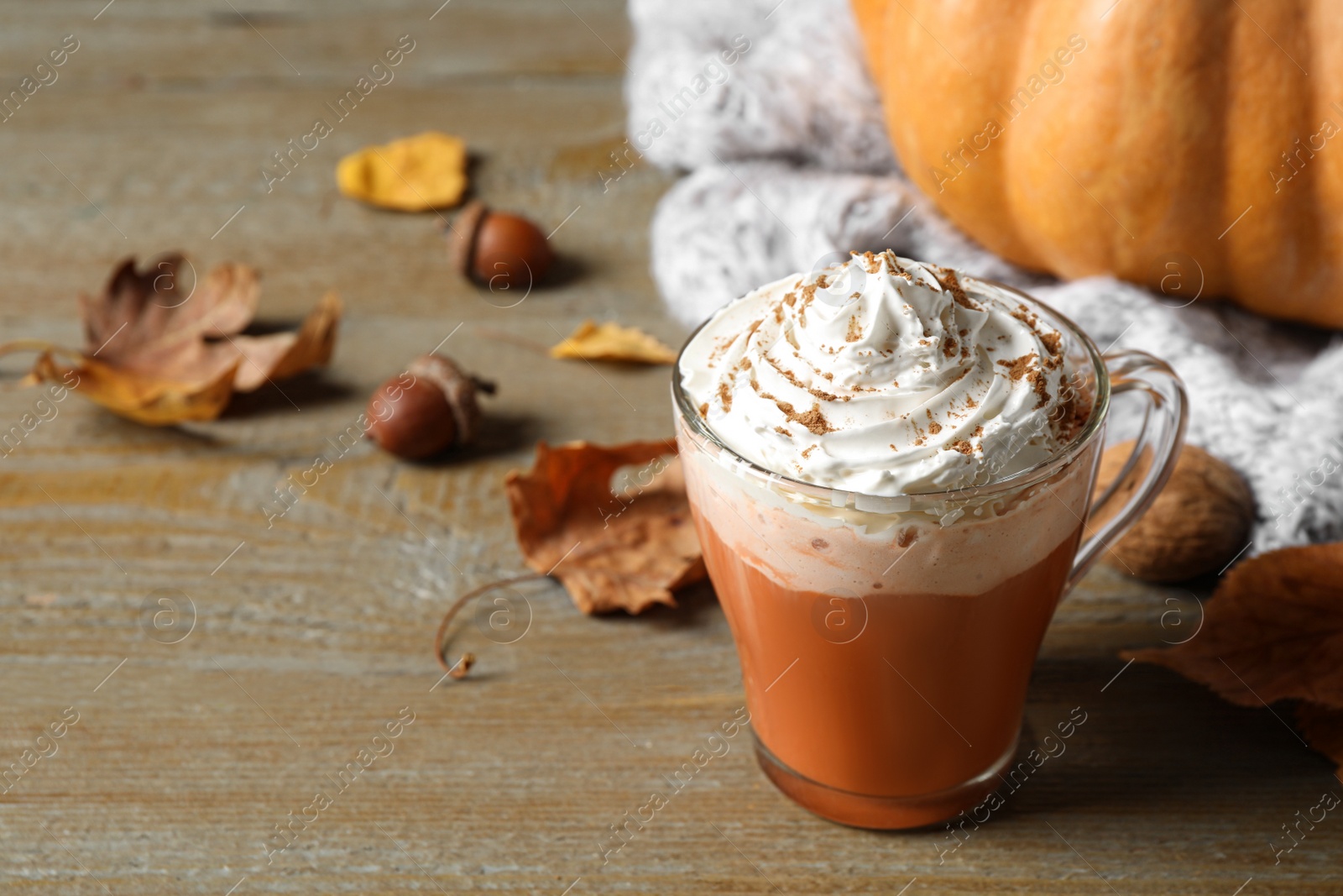 Photo of Pumpkin spice latte with whipped cream in glass cup on wooden table. Space for text