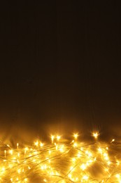 Beautiful glowing Christmas lights on wooden table, top view. Space for text