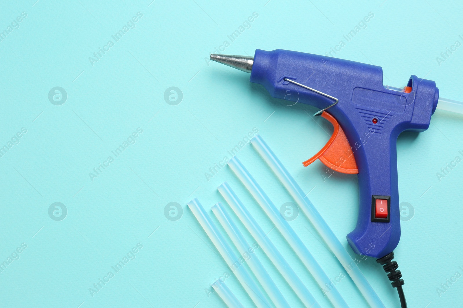 Photo of Blue glue gun and sticks on turquoise background, flat lay. Space for text