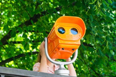 Photo of Girl looking through mounted binoculars outdoors on sunny day