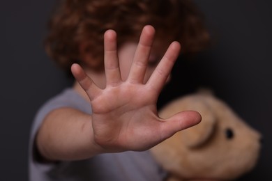Photo of Child abuse. Boy with toy making stop gesture near grey wall, selective focus