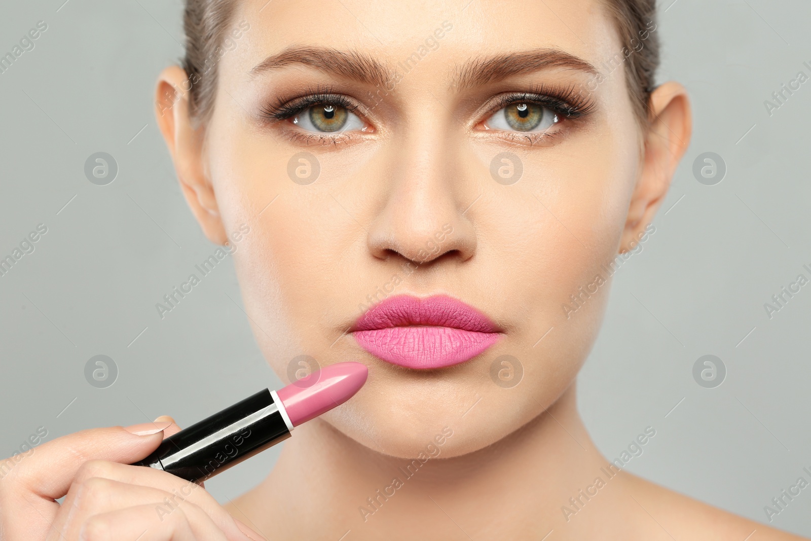 Photo of Young woman applying beautiful lipstick on gray background