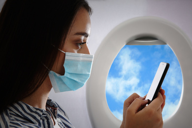 Image of Traveling by airplane during coronavirus pandemic. Woman with face mask and phone near porthole