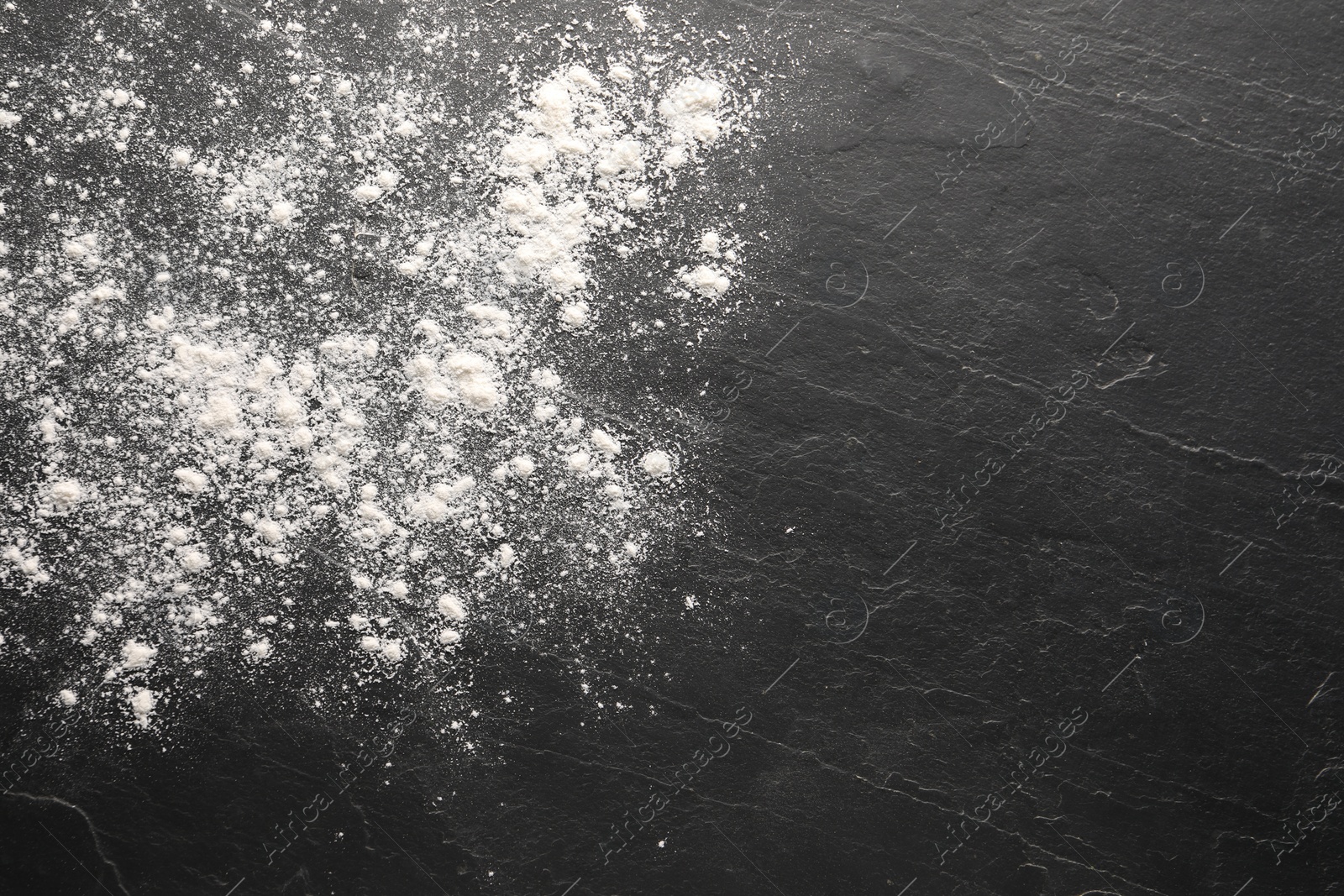 Photo of Scattered flour on black textured table, top view. Space for text