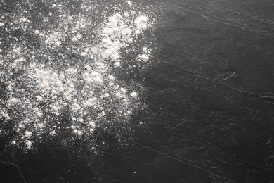 Scattered flour on black textured table, top view. Space for text