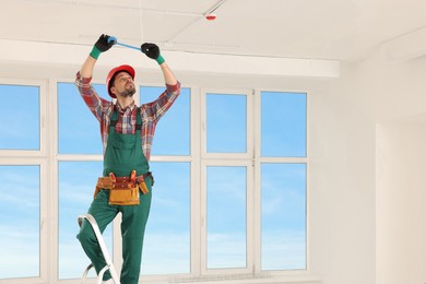 Photo of Electrician in uniform with insulating tape repairing ceiling wiring indoors