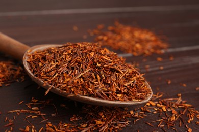 Spoon with dry rooibos leaves on wooden table, closeup