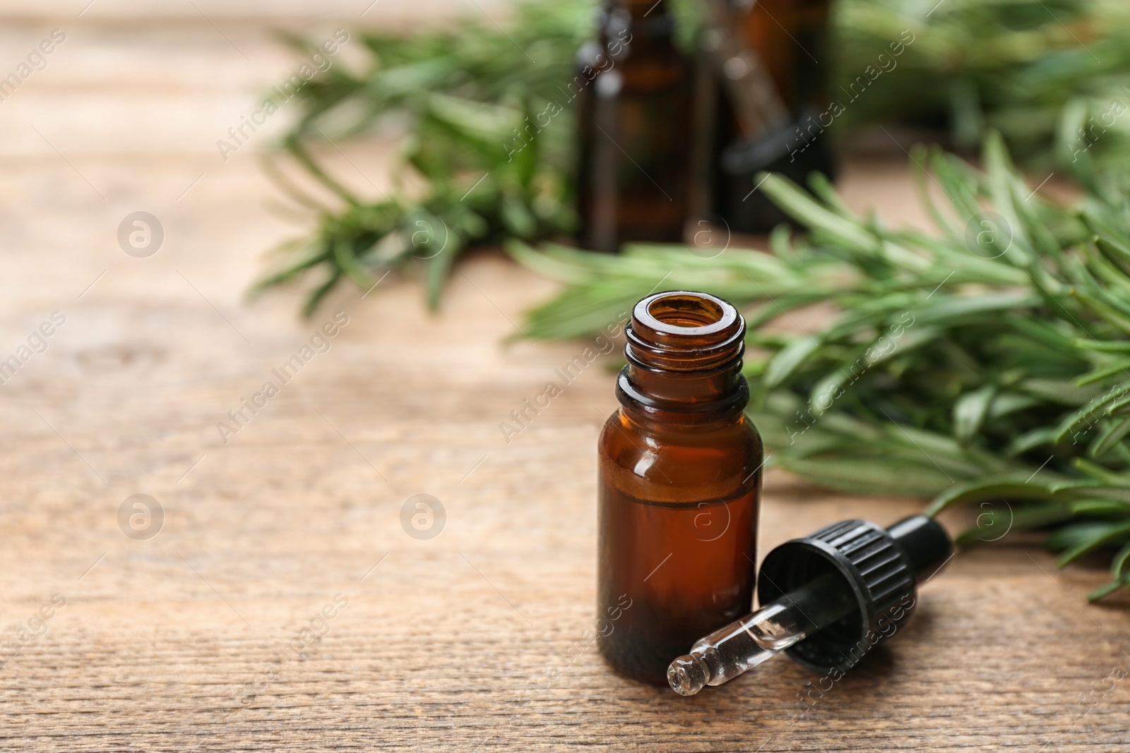 Photo of Bottle of rosemary essential oil on wooden table. Space for text