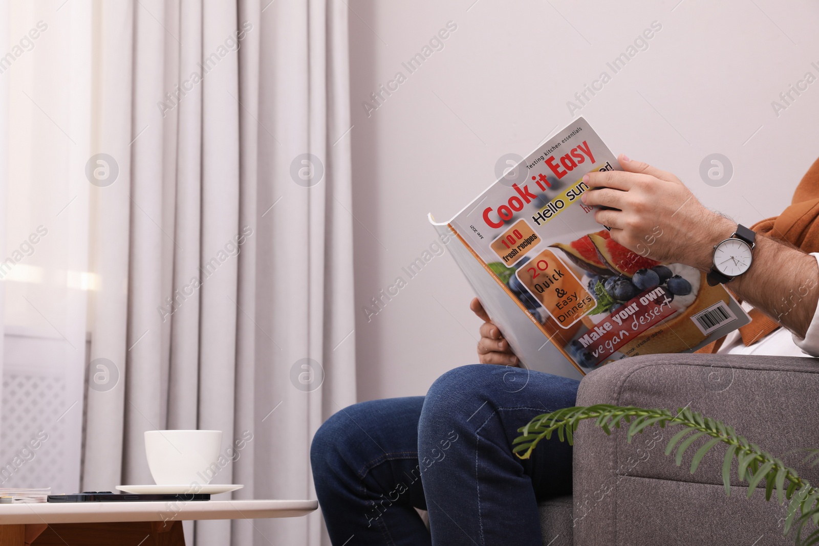 Photo of Man reading magazine in armchair at home, closeup