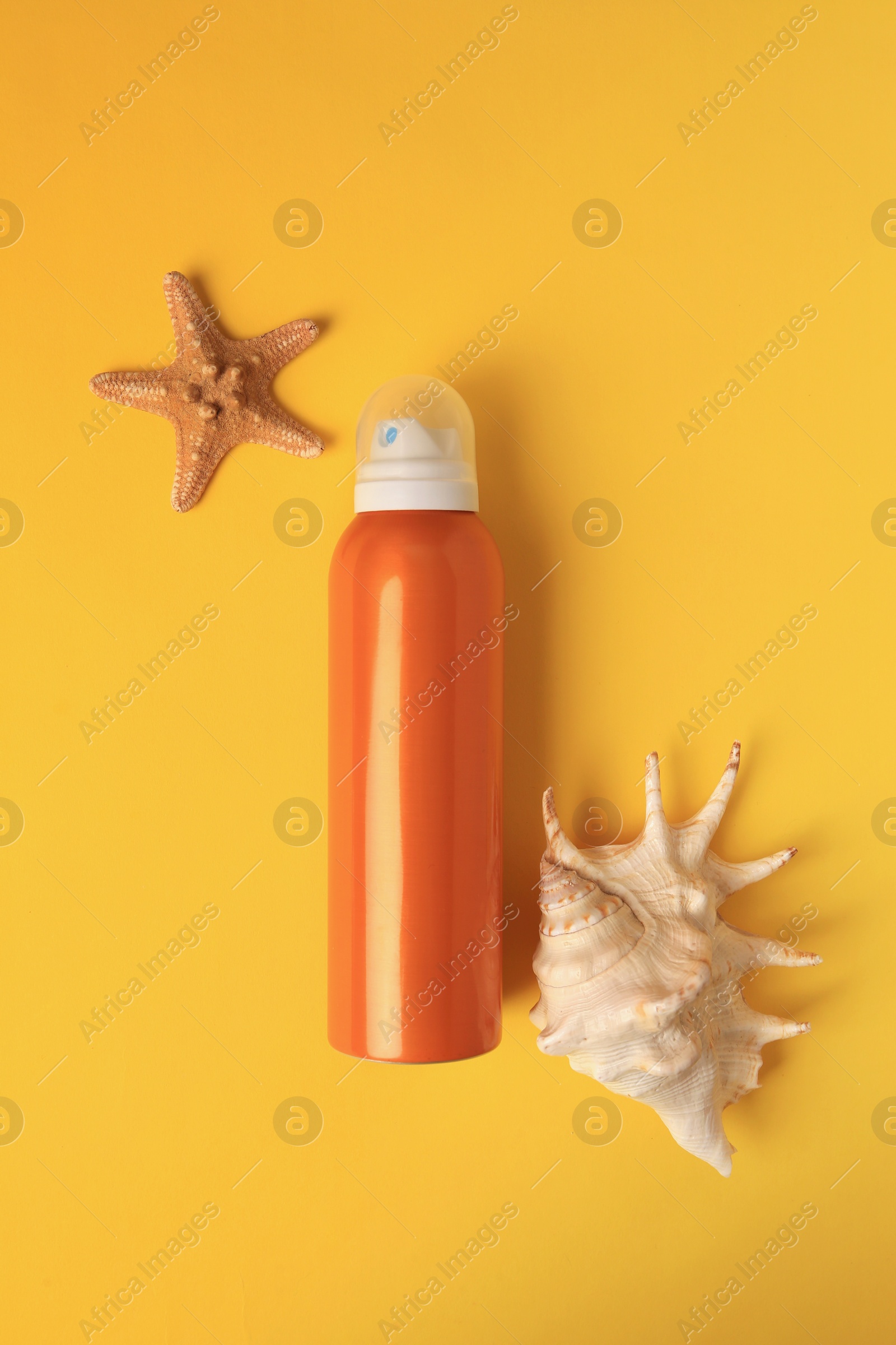 Photo of Bottle of sunscreen, starfish and seashell on yellow background, flat lay