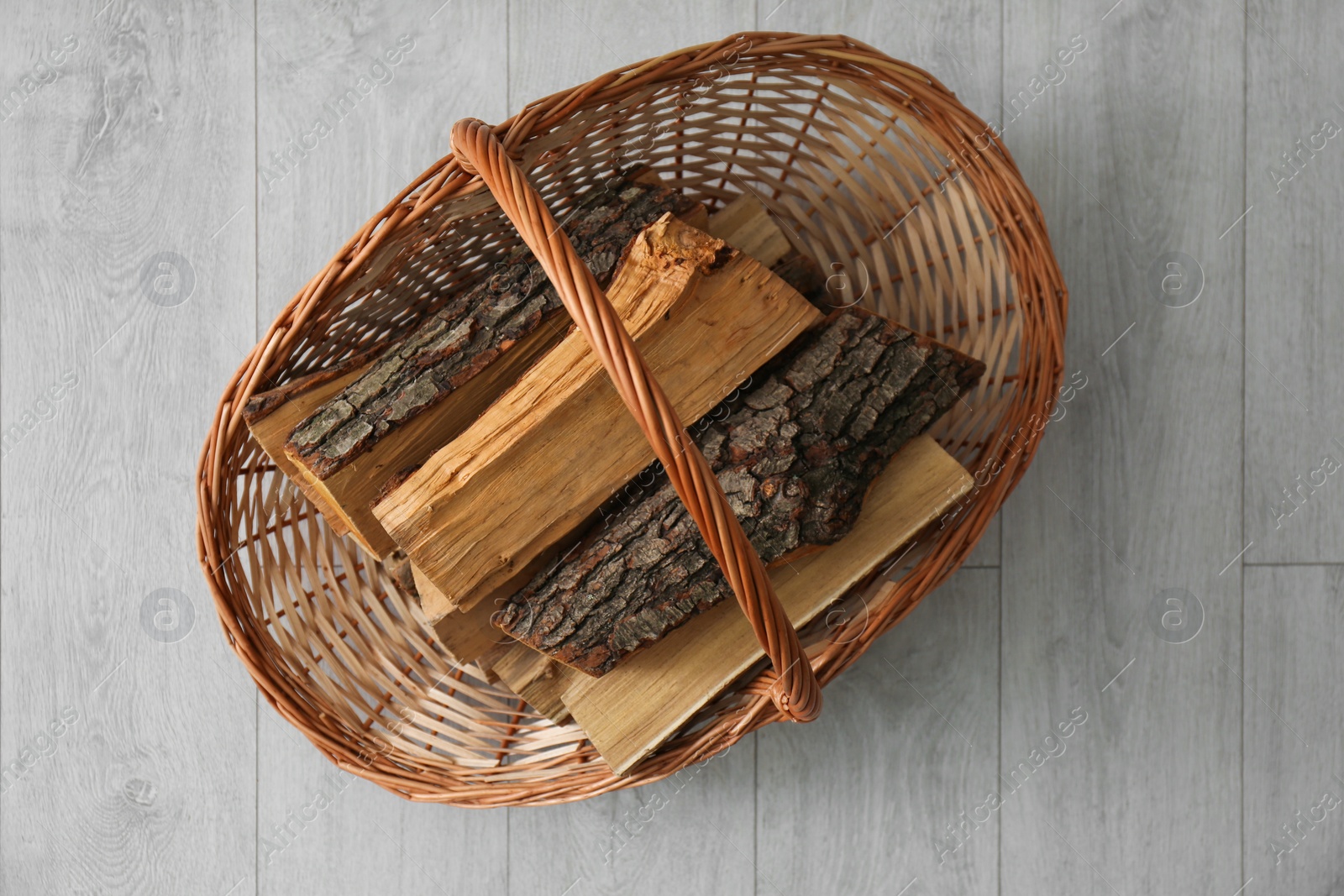 Photo of Wicker basket with firewood on floor indoors, top view