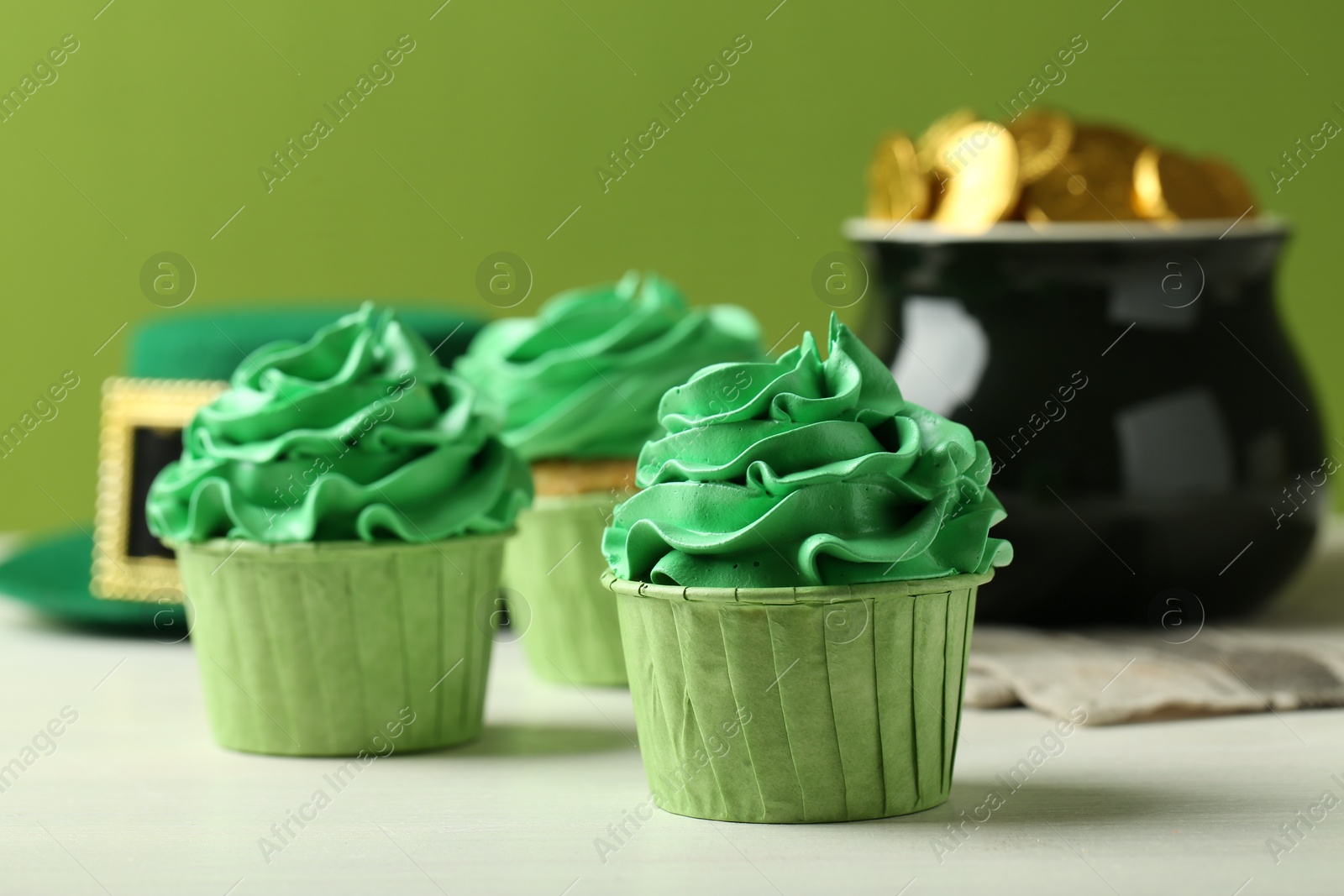 Photo of St. Patrick's day party. Tasty cupcakes with green cream, pot of gold and leprechaun hat on white table, closeup