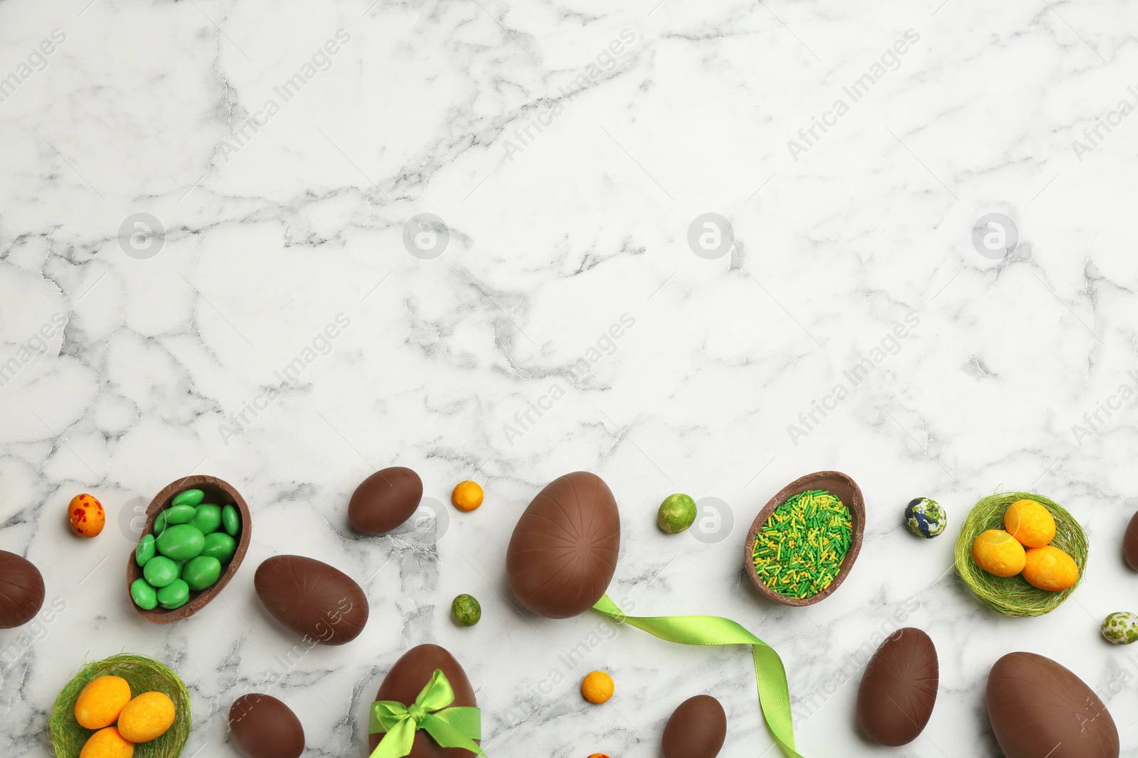 Photo of Sweet chocolate eggs and candies on white marble table, flat lay. Space for text