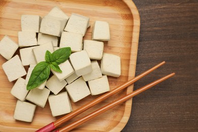 Delicious tofu with basil and chopsticks on wooden table, top view