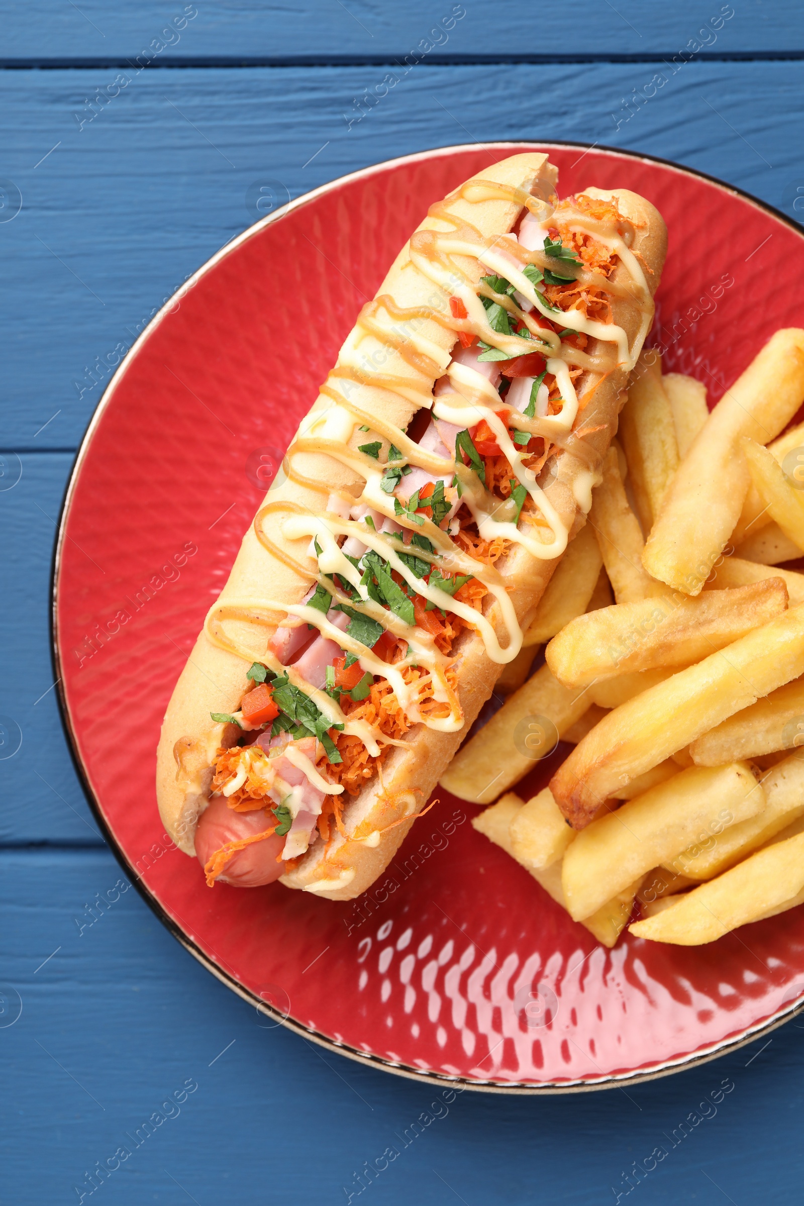 Photo of Delicious hot dog with bacon, carrot, parsley and french fries on blue wooden table, top view