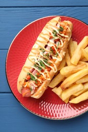 Delicious hot dog with bacon, carrot, parsley and french fries on blue wooden table, top view