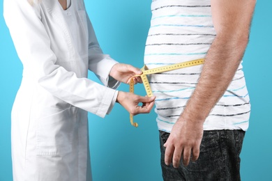 Photo of Doctor measuring fat man's waist on color background. Weight loss