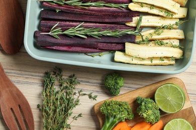 Flat lay composition with raw cut carrots in baking dish on wooden table