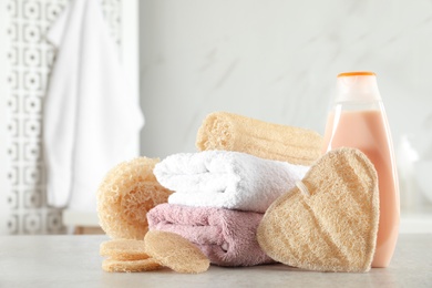 Photo of Natural loofah sponges, towels and bottle with cosmetic product on table in bathroom