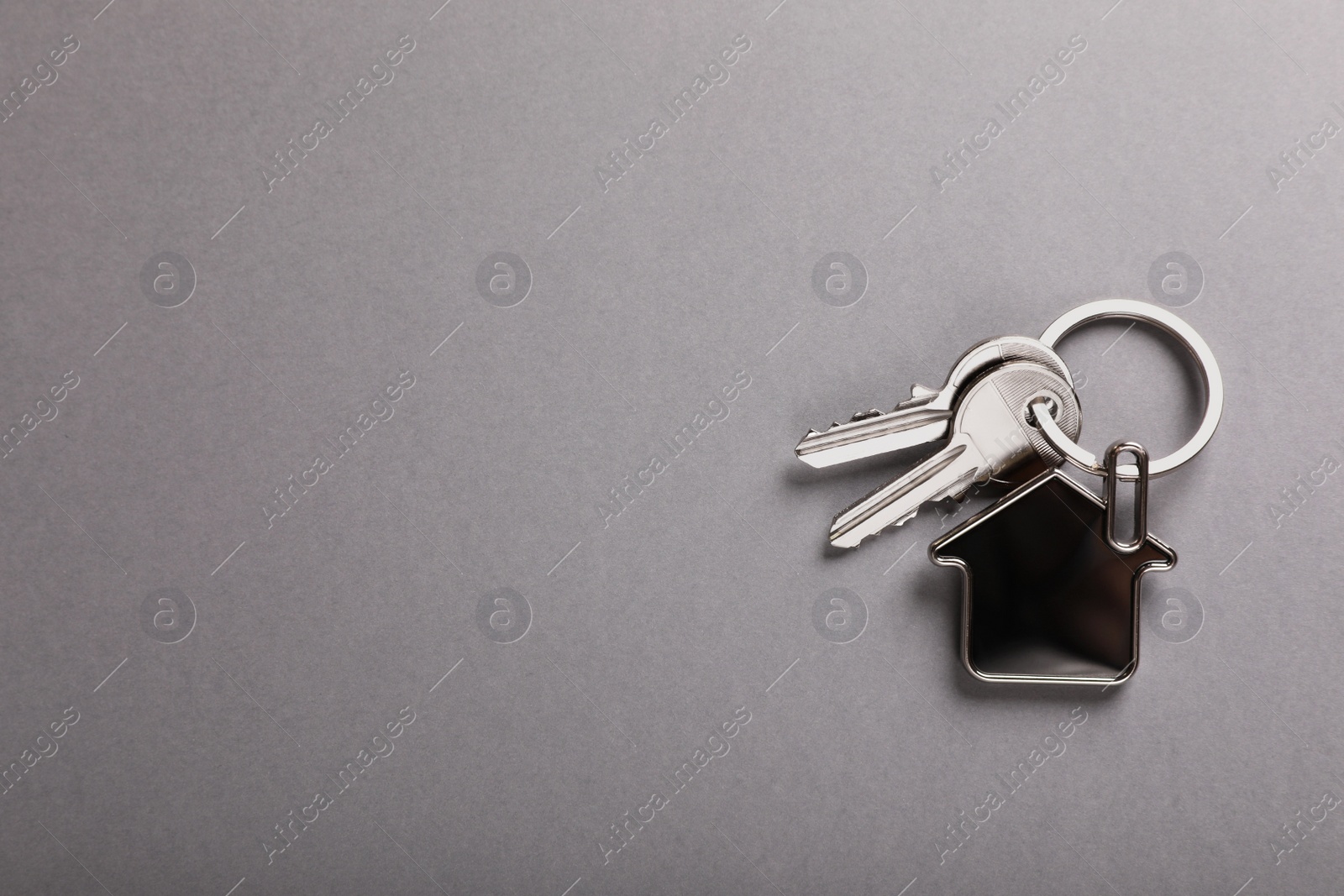 Photo of Keys with trinket in shape of house on grey background, top view and space for text. Real estate agent services