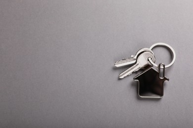 Photo of Keys with trinket in shape of house on grey background, top view and space for text. Real estate agent services