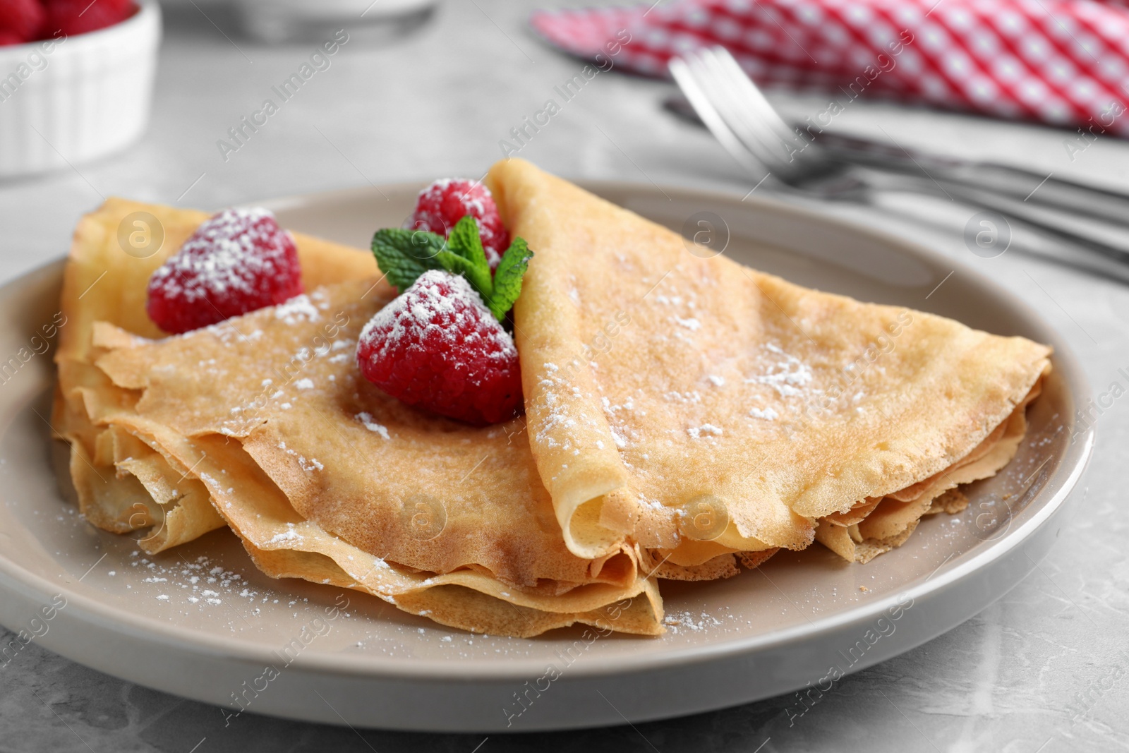 Photo of Delicious crepes served with mint, raspberries and powdered sugar on grey table, closeup