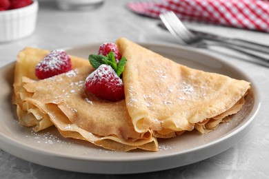 Photo of Delicious crepes served with mint, raspberries and powdered sugar on grey table, closeup