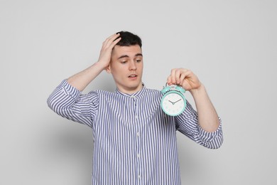 Emotional young man with alarm clock on light grey background. Being late concept