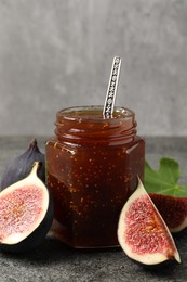 Photo of Glass jar with tasty sweet jam and fresh figs on grey textured table, closeup