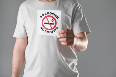 Photo of Man holding card with no smoking sign on gray background, closeup