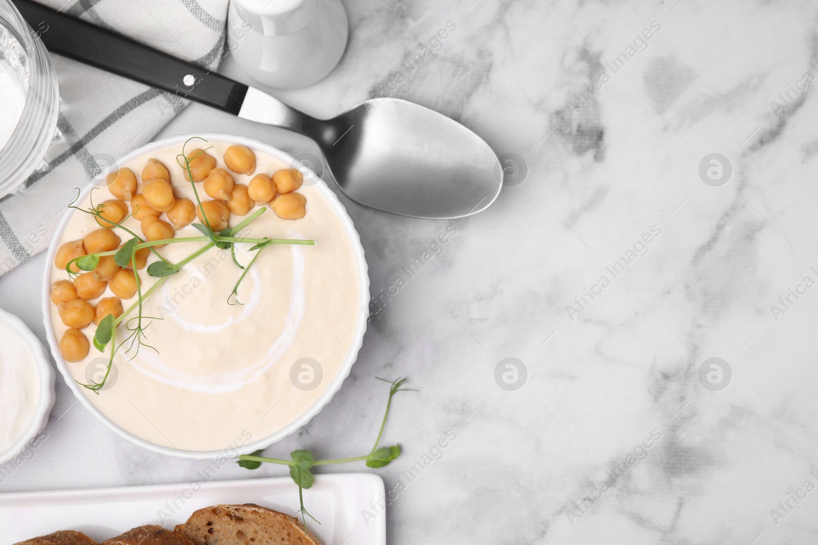 Photo of Flat lay composition of tasty chickpea soup in bowl, sauce and bread served on white marble table. Space for text