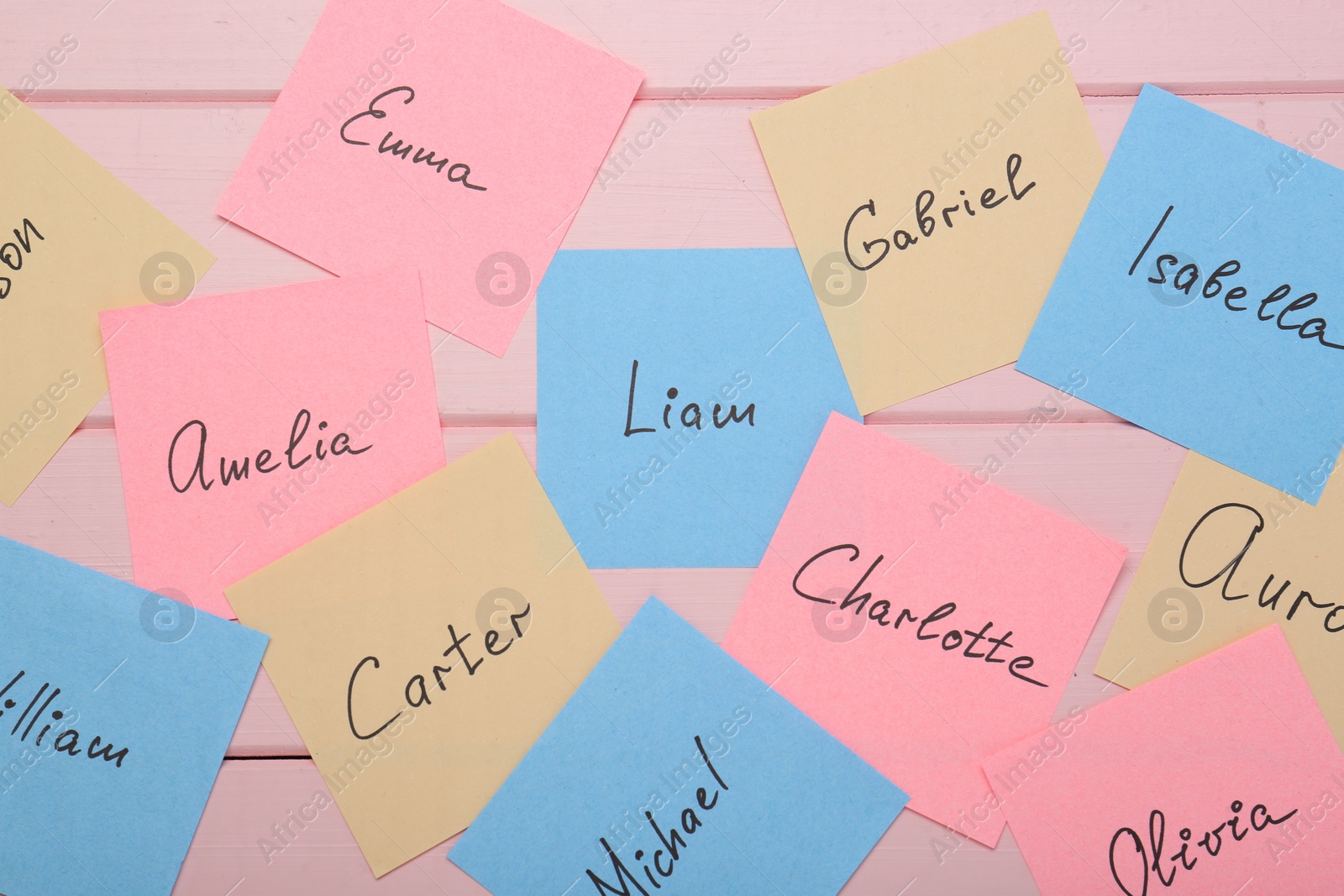 Photo of Paper stickers with different names on pink wooden background, flat lay. Choosing baby's name