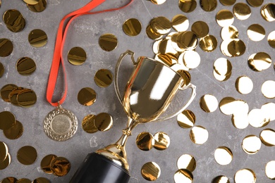 Photo of Gold trophy cup, medal and confetti on grey stone background, flat lay