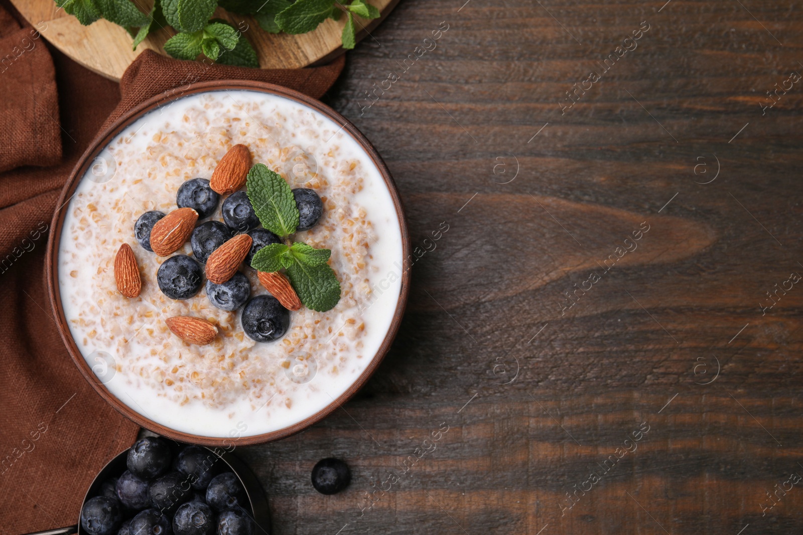 Photo of Tasty wheat porridge with milk, blueberries and almonds in bowl on wooden table, flat lay. Space for text