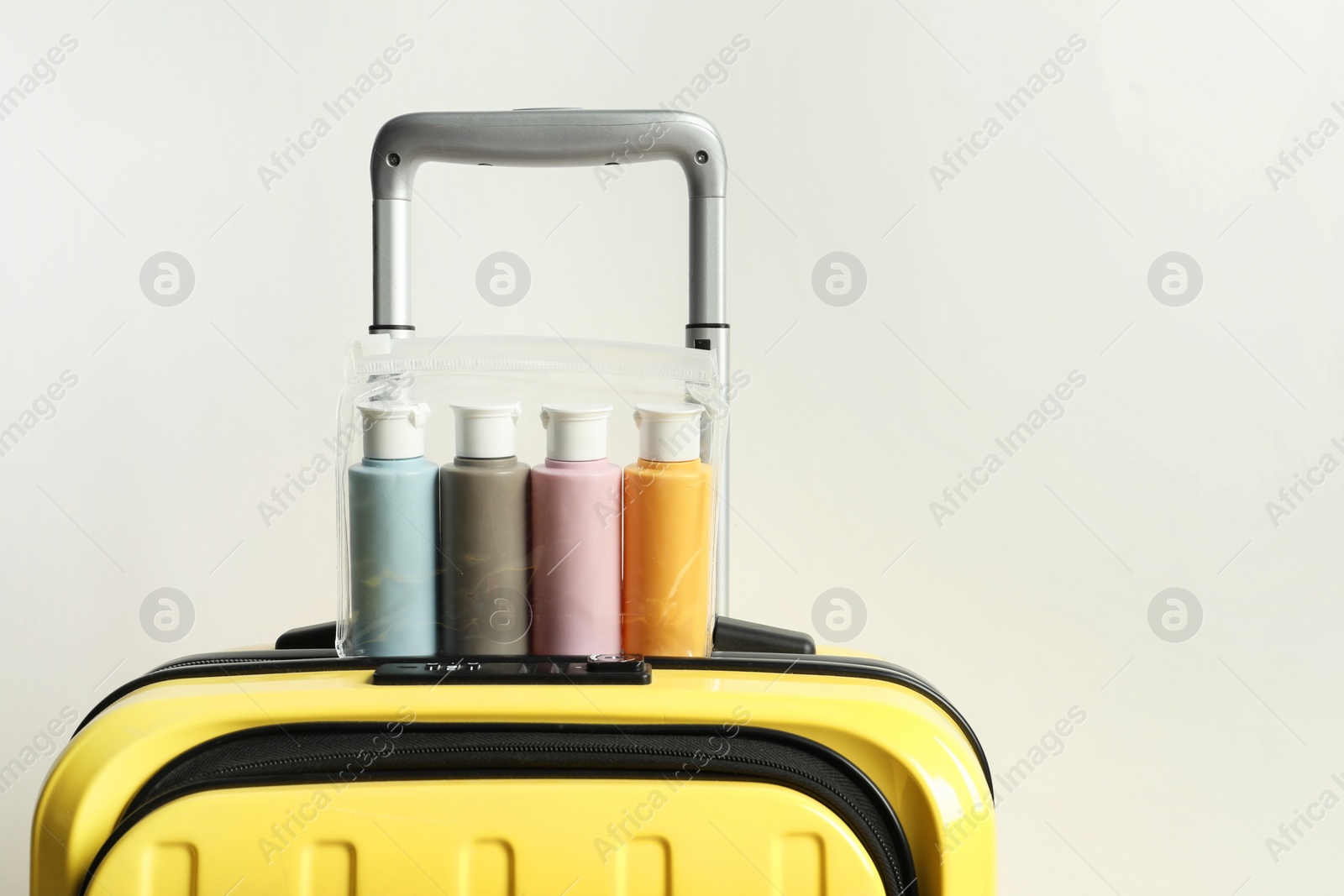 Photo of Cosmetic travel kit in plastic bag on suitcase against light background, space for text