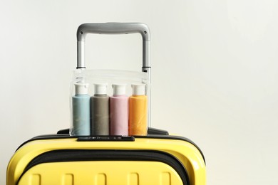 Photo of Cosmetic travel kit in plastic bag on suitcase against light background, space for text