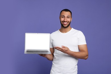 Smiling young man showing laptop on lilac background