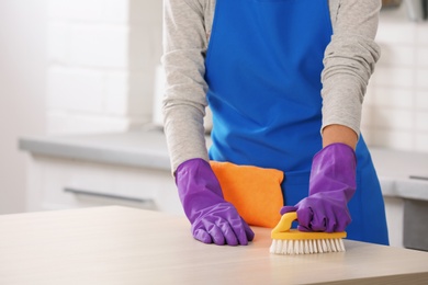 Photo of Woman cleaning table with brush in kitchen, closeup. Space for text