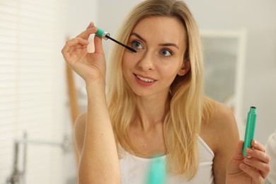 Photo of Beautiful woman with brush applying mascara in bathroom