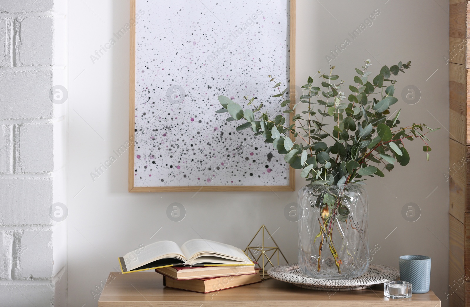 Photo of Beautiful eucalyptus branches and books on table in modern room. Interior design