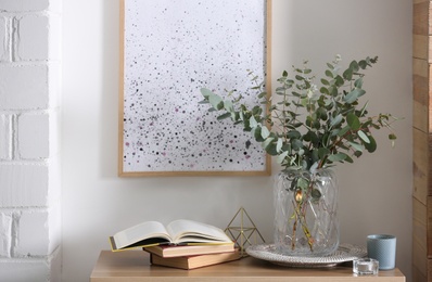 Beautiful eucalyptus branches and books on table in modern room. Interior design