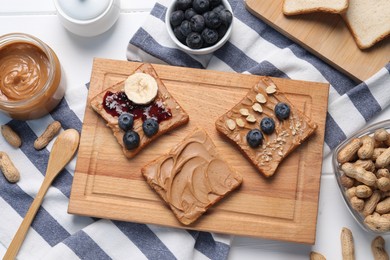 Photo of Different tasty toasts with nut butter and products on white wooden table, flat lay